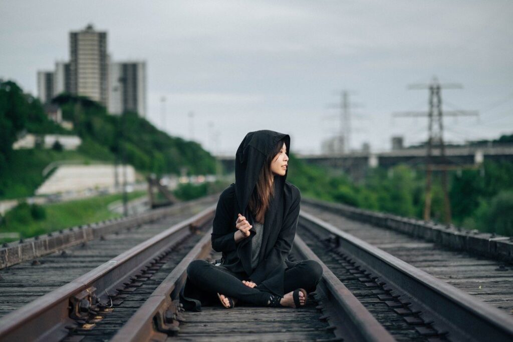 A traveler with a China tourist visa sits on the railway tracks, looking to her right for travel advice.